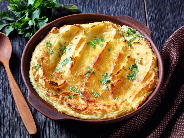 Schale mit gebackenem Kartoffelpüree auf dunklem Untergrund.