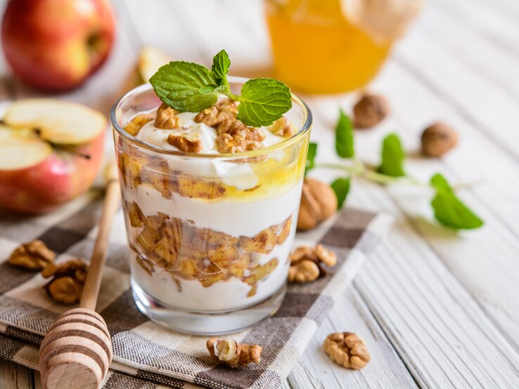 Herbst-Dessert im Glas mit Apfel, Walnuss, Quark und Honig auf hellem Holz.