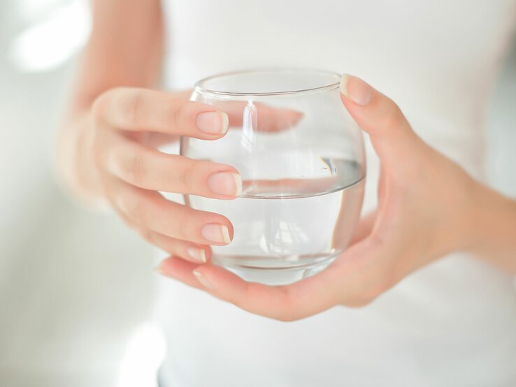 Frau hält Glas Wasser in den Händen. Insbesondere auf die Ernährung vor einer Darm- oder Magenspiegelung sollten Sie achten.
