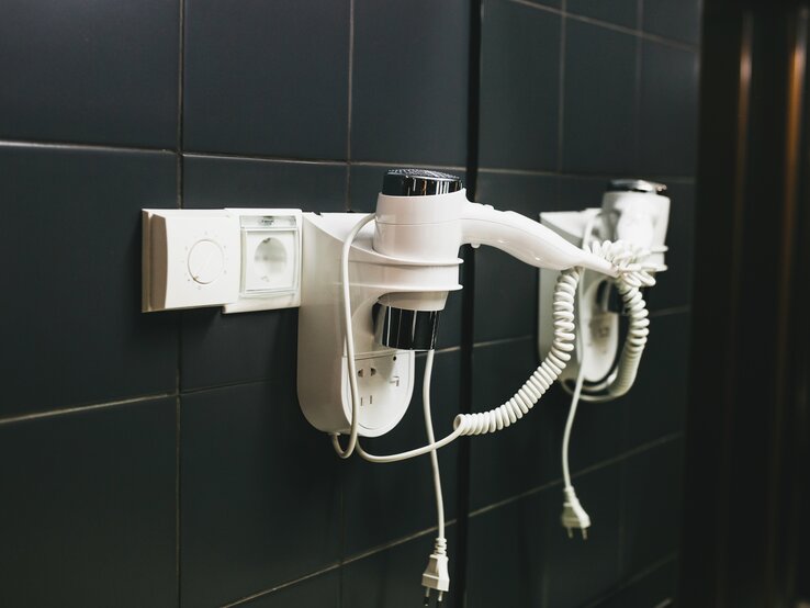 Viele Hotels stellen Gästen einen Föhn zur Verfügung. Eigentlich praktisch. Wir verraten Ihnen, warum Sie den Hotel-Föhn besser nicht benutzen sollten. Ein Föhn hängt im Hotelzimmer an der Wand.