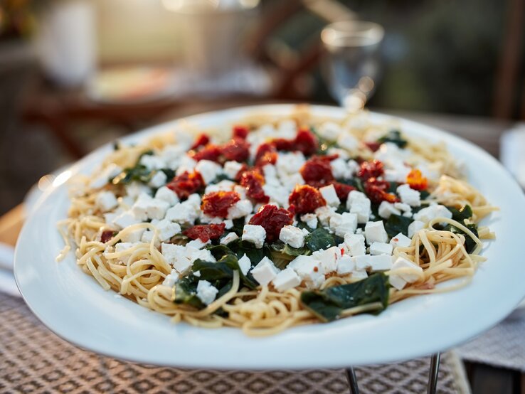 Spaghetti mit Spinat, Feta und getrockneten Tomaten auf weißem Teller. 