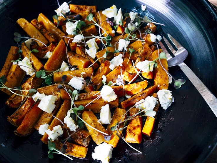 Suesskartoffelsalat-Feta Eine schwarze Schüssel mit dem Süßkartoffelsalat und Feta nah fotografiert auf einem dunklen Holztisch.