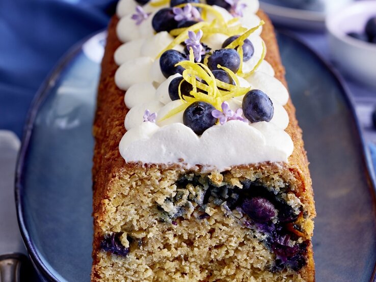 Eines unserer Lieblingsrezepte: Heidelbeer-Haferflocken-Kuchen Auf einem Teller steht ein Heidelbeer-Haferflocken-Kuchen. Er ist mit Sahne und Blaubeeren dekoriert.