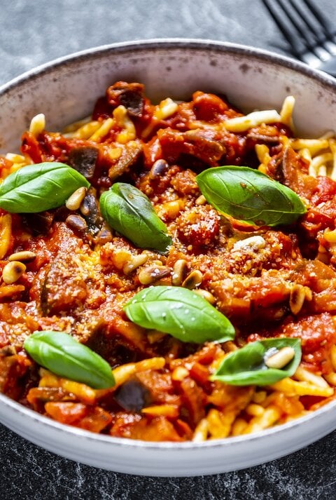 Ein Teller Pasta mit Frischkäsesoße, Basilikum und Pinienkernen, daneben liegt eine Gabel.