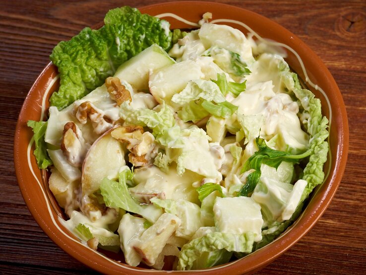 Eine braune Schale mit dem Salat auf einem dunklen Holztisch von oben fotografiert.