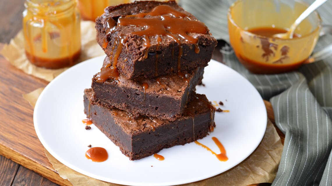 Ein Teller mit Salzkaramell-Brownies auf einem Holzbrett.