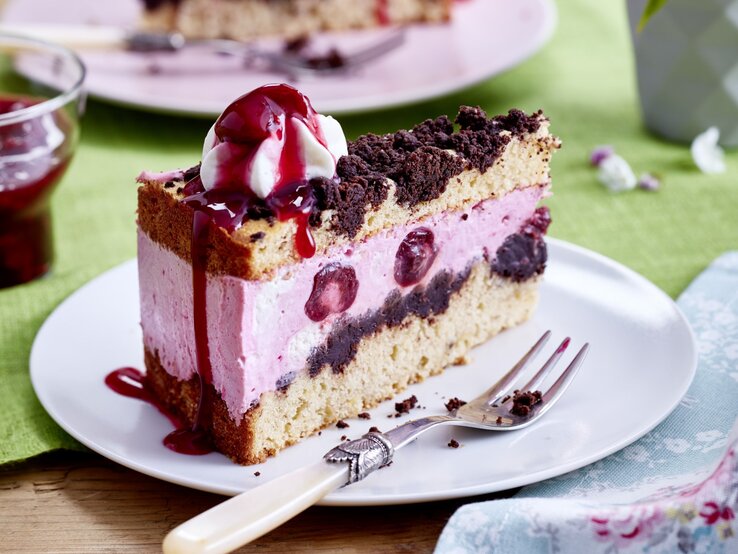 Diese leckere Kiba-Streuseltorte vereint Kirschen, Banane und Schokolade zu einem cremigen Genuss. Auf einem Teller steht ein Stück Kiba-Streuseltorte. Es ist mit einem Klecks Schlagsahne verfeinert.