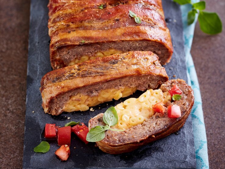 Auf einem Steinbrett ist ein Hackbraten mit Makkaroni-Füllung angerichtet. Er ist braun gebraten und sieht knackig aus.