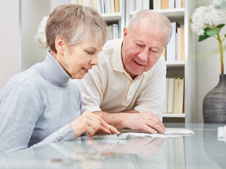 Ein älteres Ehepaar sitzt am Tisch und checkt Dokumente mit einem Taschenrechner.