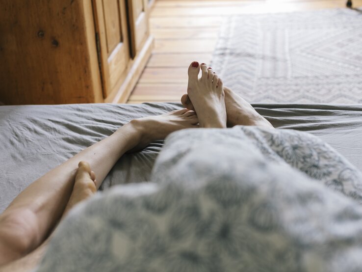 Füße von Mann und Frau im Bett zu sehen