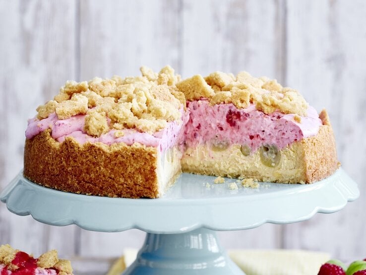 Diese fruchtige Stachelbeer-Quark-Streuseltorte bringt Erfrischung mit! Genau das Richtige für die sonnigen Tage. Auf einer Etagerie steht eine Stachelbeer-Quark-Streuseltorte. Sie ist mit einer rosa Creme gefüllt und angeschnitten.