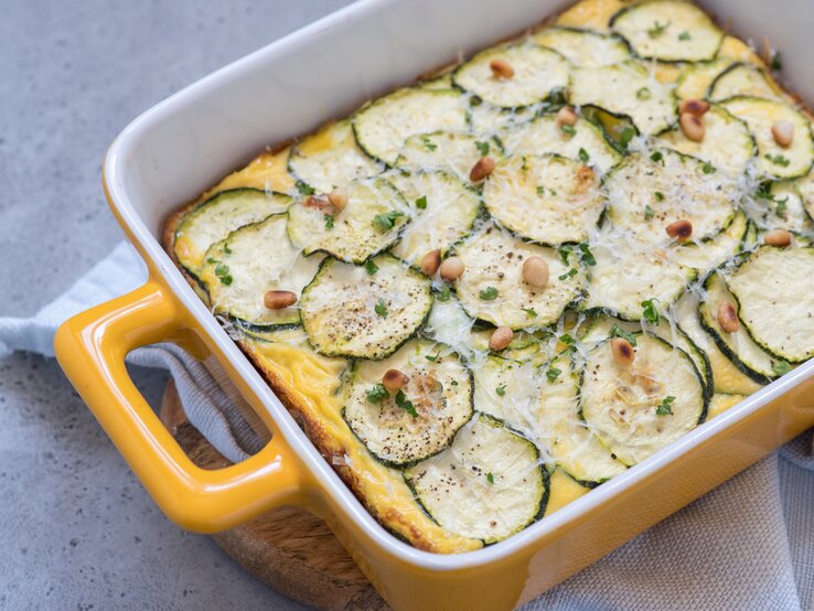 Zucchini-Auflauf mit Hackfleisch und Feta in gelber Auflaufform auf hellem Untergrund. 