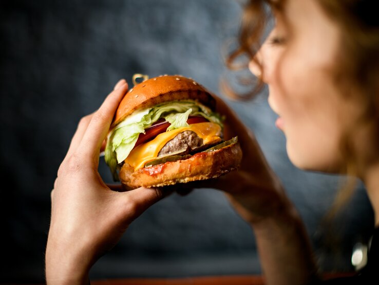 Stiftung Warentest prüft vegetarische und vegane Burger-Pattys: Close-up einer Frau, die einen Burger in den Händen hält. 