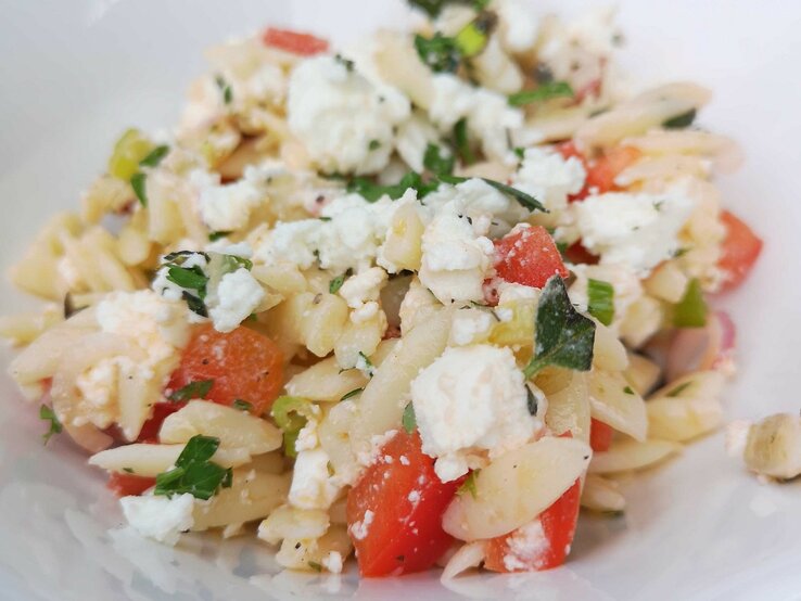 Griechischer Nudelsalat mit Feta, Melone, Tomate und Oliven auf weißem Teller. 