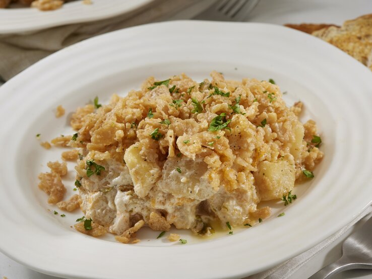 Käsiger Kartoffel-Rösti-Auflauf mit Petersilie bestreut auf einem weißen Teller. 