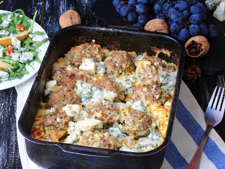 Herzhafter Hackbällchen-Auflaufs in cremiger Gorgonzola-Soße, serviert in einer schwarzen, ofenfesten Form. Die Hackbällchen sind gleichmäßig in der goldbraunen, cremigen Käsesoße verteilt.