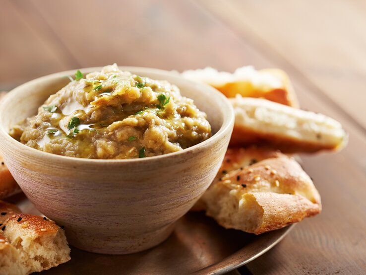 Lib el Kousa ist ein Zucchini-Knoblauch-Dip, der sich bestens als Beilage zum Grillen eignet. Eine Schale Lib el Kousa, ein levantinischer Zucchini-Knoblauch-Dip, auf einem Tablett, darauf außerdem Fladenbrot-Stücke.