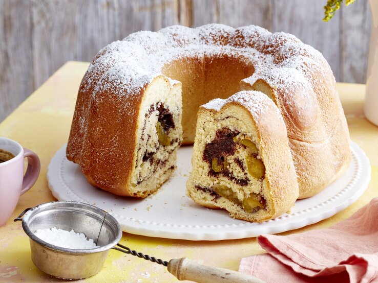 Mit dem Mohn-Hupf mit Mirabellen bringst du einen Hauch von Frische und Fruchtigkeit auf deine Kaffeetafel. Auf einem Teller steht ein Mohn-Hupf mit Mirabellen. Er ist mit Puderzucker bestreut und fluffig im Inneren.