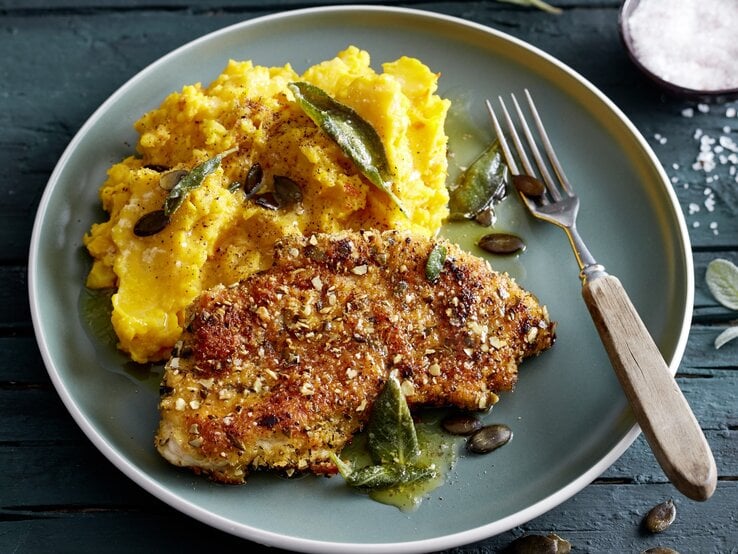 Knusper-Schnitzel mit Kürbisstampf auf Teller, belegt mit Salbei und Kürbiskernen. 