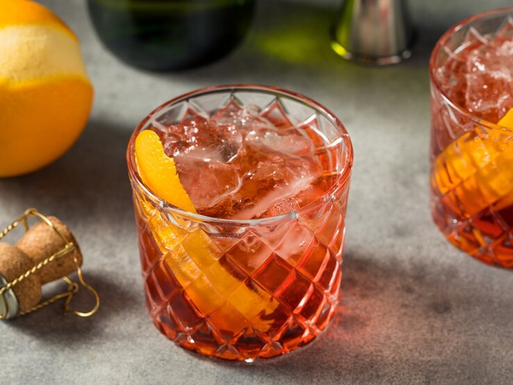 Zwei Gläser mit dem falschen Negroni auf einem Steintisch mit Prosecco und einer Orange.