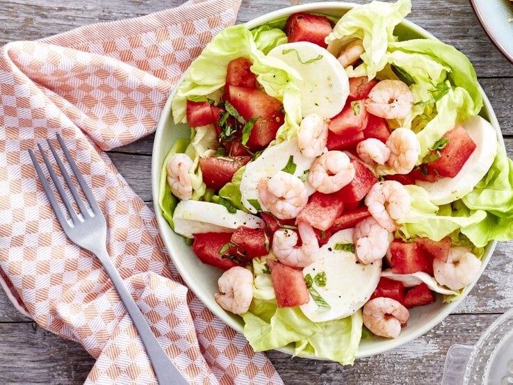 In einer Schüssel ist ein Wassermelonen-Salat mit Mozzarella angerichtet. Er ist mit Garnelen garniert.