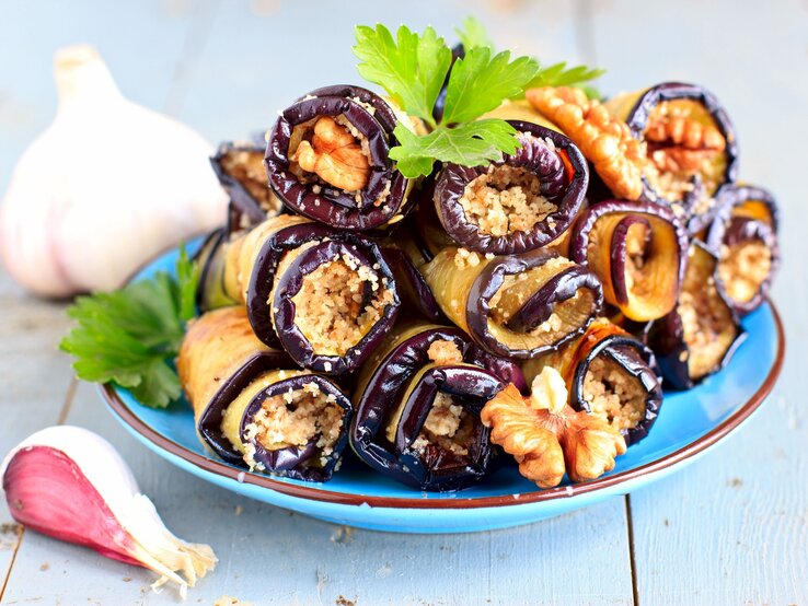 Badridschani, gefüllte Auberginen-Walnuss-Röllchen, auf einem Teller zu einer Pyramide gestapelt, daneben liegt Knoblauch.