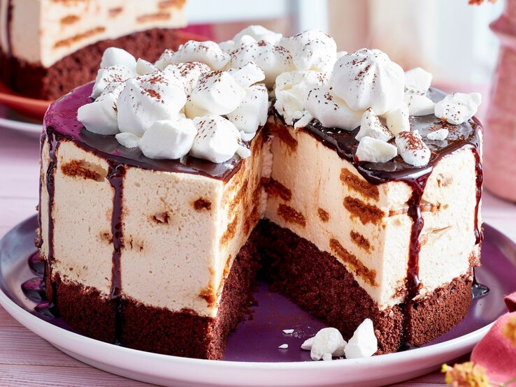 Schoko-Tiramisu-Torte Auf einem Teller liegt eine angeschnittene Schoko-Tiramisu-Torte. Man erkennt die unterschiedlichen Schichten. Sie ist getoppt mit Baisertuffs und Schokoladensoße.