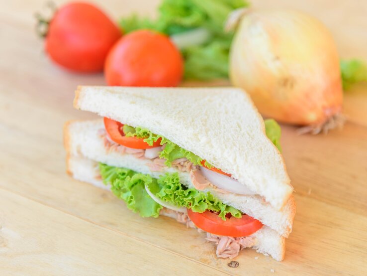 Draufsicht, schräg: Ein Thunfisch-Tramezzini mit Tomate auf einem hellem Untergrund aus Holz.