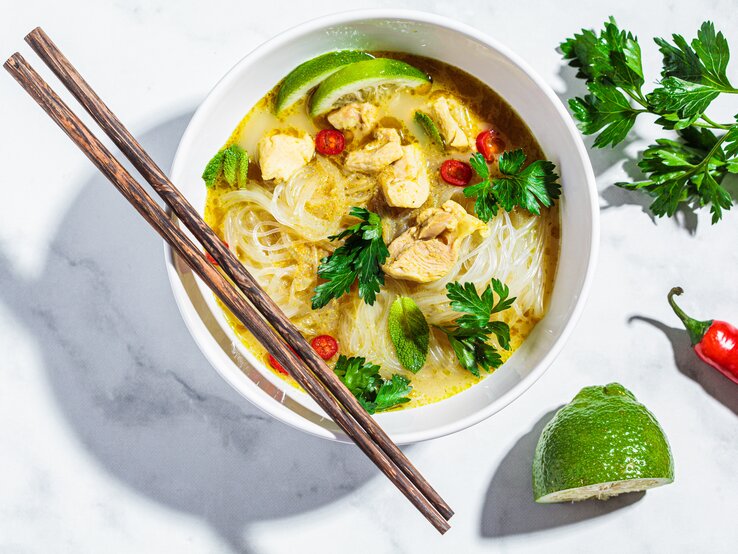 Eine weiße Schüssel mit Thai-Currysuppe mit Nudeln auf einem weißen Tisch.