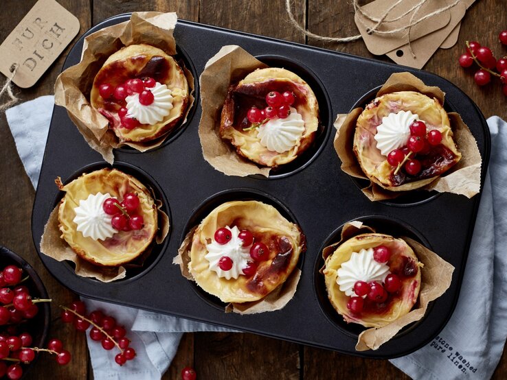 Johannisbeer-Mandel-Törtchen in einer Muffinform. Daneben liegen Johannisbeeren und ein Küchentuch. 