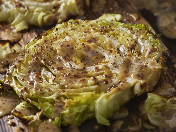 Gebackene Kohl-Steaks an Senf-Soße auf Holzbrett.