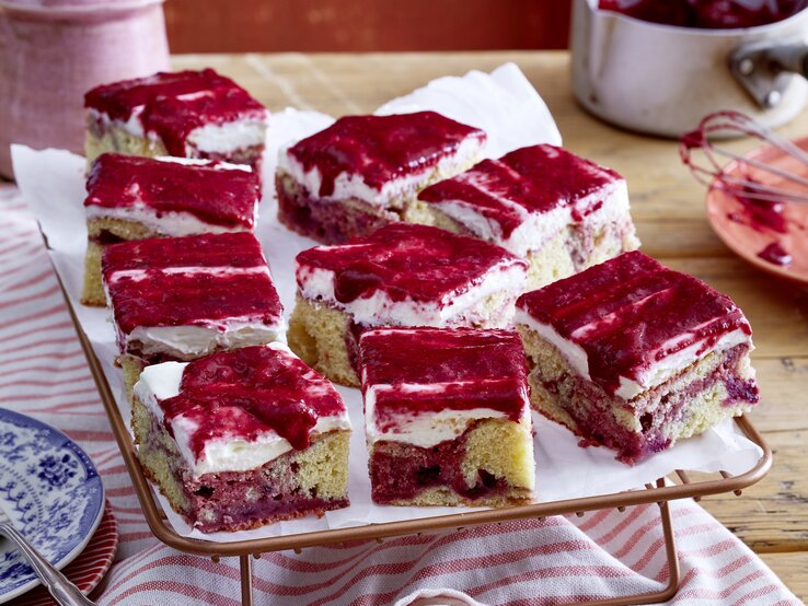 Beeren-Marmorkuchen vom Blech mit cremiger Frischkäseglasur, in Würfel geschnitten auf einem weißen Tuch. 