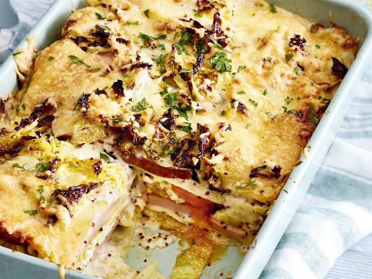 In einer Auflaufform ist eine Fleischkäse-Lasagne mit Wirsingrahm angerichtet. Sie ist mit Kräutern überstreut.