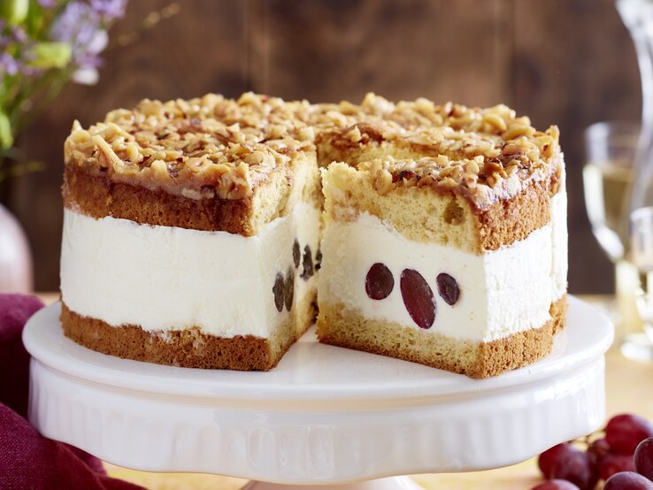 Angeschnittene Weißwein-Trauben-Torte auf weißem Tortenteller, verschwommener Hintergrund. 