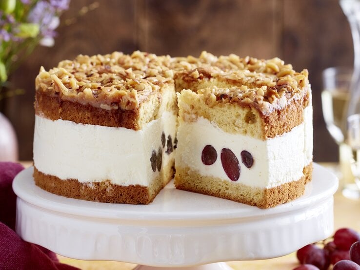 Angeschnittene Weißwein-Trauben-Torte auf weißem Tortenteller, verschwommener Hintergrund. 