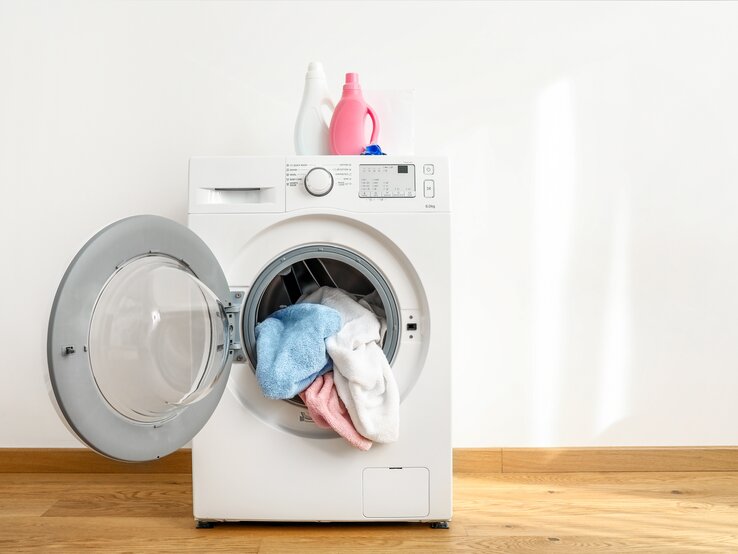 Eine Waschmaschine mit geöffneter Tür. Darin liegt gewaschene Wäsche.