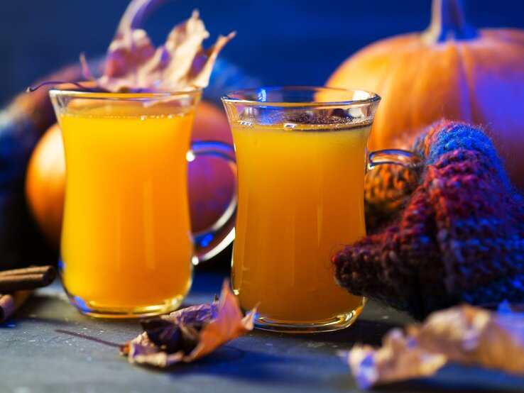 Halloween-Bowle Zwei Gläser der gelben Bowle vor Kürbissen und blauem Hintergrund.