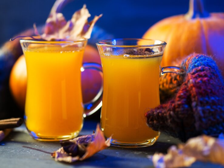 Halloween-Bowle Zwei Gläser der gelben Bowle vor Kürbissen und blauem Hintergrund.