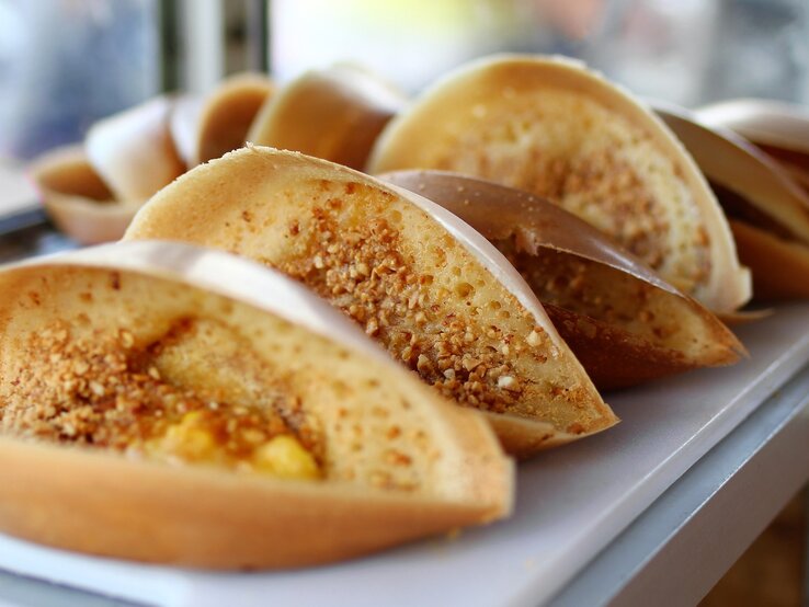 Mehrere Erdnusspfannkuchen zusammengeklappt auf einem Tisch und im Hintergrund unscharf helle Fenster zu sehen.