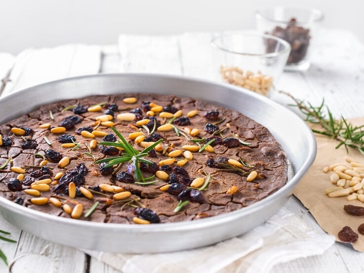 Eine weiße Platte mit toskanischem Kastanienmehlkuchen auf weißem Holztisch.