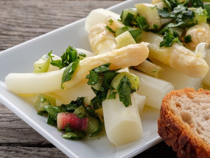 Ein weißer rechteckiger Teller mit dem Spargelsalat auf einem dunklen Holztisch.