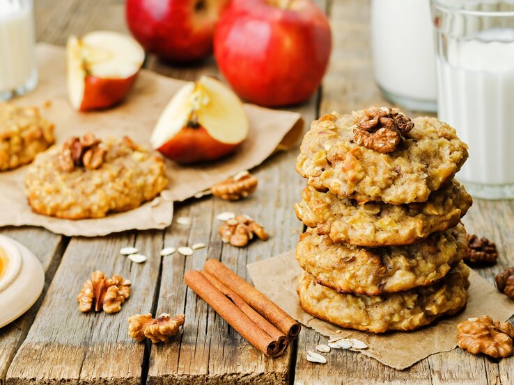 Die Apfel-Haferkekse mit Zimt sind die perfekte Ergänzung für die Keksdose. Ein Tisch mit Apfel-Haferkeksen mit Zimt neben einem Glas Milch.