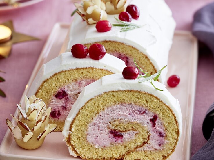 Auf einem Teller liegt eine  Marzipan-Cranberryrolle. Sie ist mit frischen Beeren und Marzipan verziert.