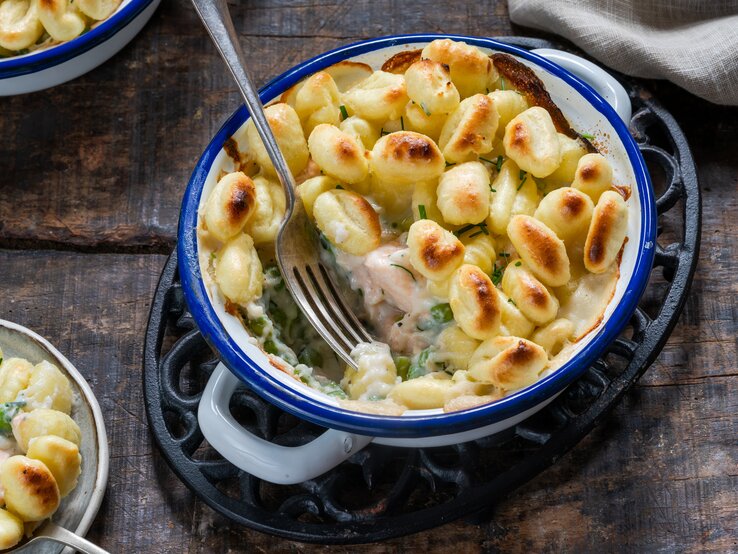 Gnocchi-Lachsauflauf-Erbsen Eine blaue Form mit Gnocchi-Lachsauflauf mit Erbsen auf einem braunen Tisch.