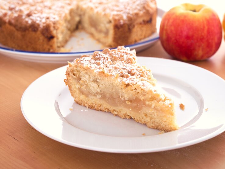 Ein Stück Apfelkuchen mit Streusel auf einem weißen Teller. 