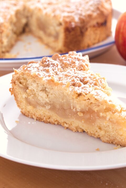 Ein Stück Apfelkuchen mit Streusel auf einem weißen Teller. 