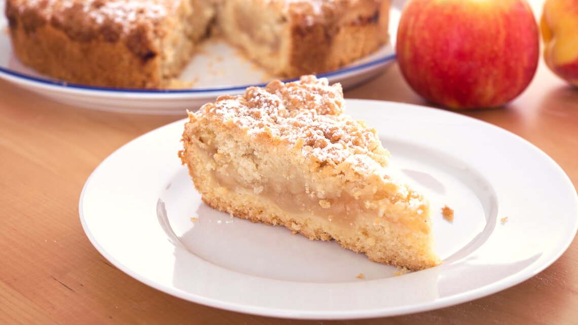 Ein Stück Apfelkuchen mit Streusel auf einem weißen Teller. 