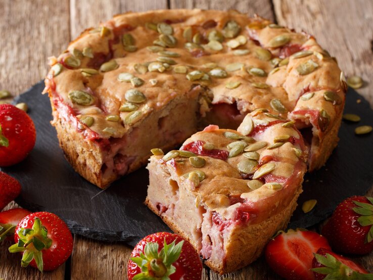 Nahaufnahme eines Erdbeer-Bananenkuchens auf schwarzer Schieferplatte und Holztisch. 