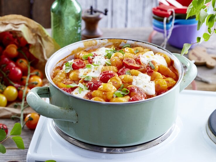 Eintopf aus Gnocchi mit Burrata und gebackenen Tomaten, bestreut mit frischem Basilikum und serviert in einem großen, hellen Kochtopf auf einem Campingtisch.  
