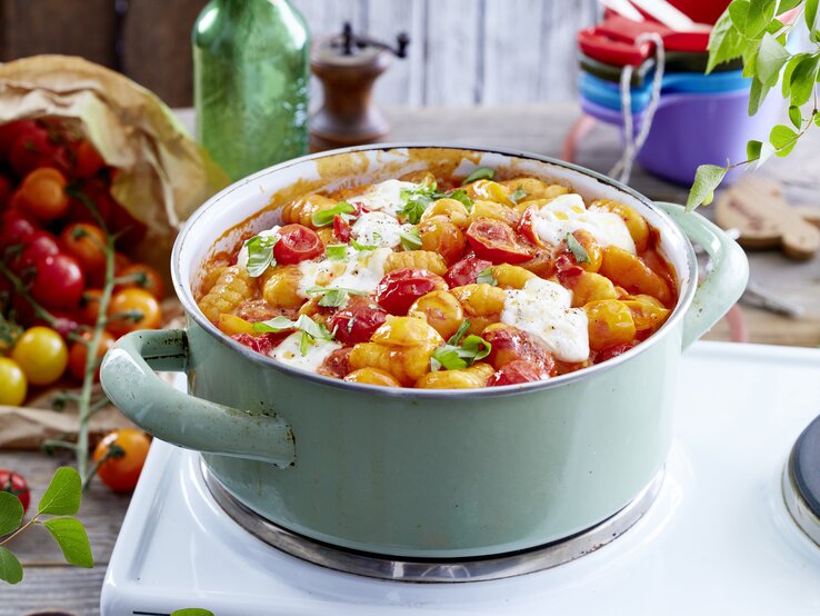 Eintopf aus Gnocchi mit Burrata und gebackenen Tomaten, bestreut mit frischem Basilikum und serviert in einem großen, hellen Kochtopf auf einem Campingtisch.  